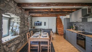 A modern kitchen with wooden beams, a stone wall, and a dining area with a table set for four. - Gorgeous home in Veprinac (Veprinac)