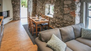 A cozy living area with a stone wall, a wooden dining table set for four, and a leather sofa with cushions. - Gorgeous home in Veprinac (Veprinac)