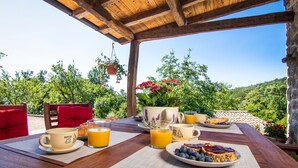 An outdoor breakfast setup with a wooden table, red chairs, and a scenic view of trees and hills. - Gorgeous home in Veprinac (Veprinac)