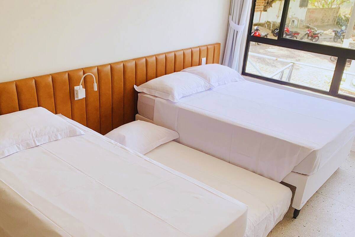 Habitación de hotel con dos camas, cabecero de madera y ventana con vista a la calle.