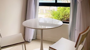 A room with a round white table, two white chairs, and a window with white curtains.