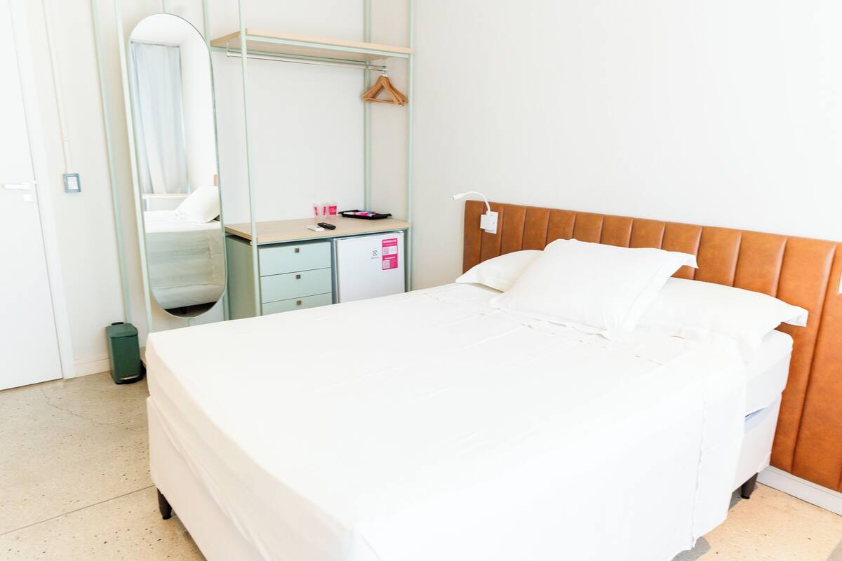 Una habitación de hotel con cama, cómoda, espejo y perchero.
