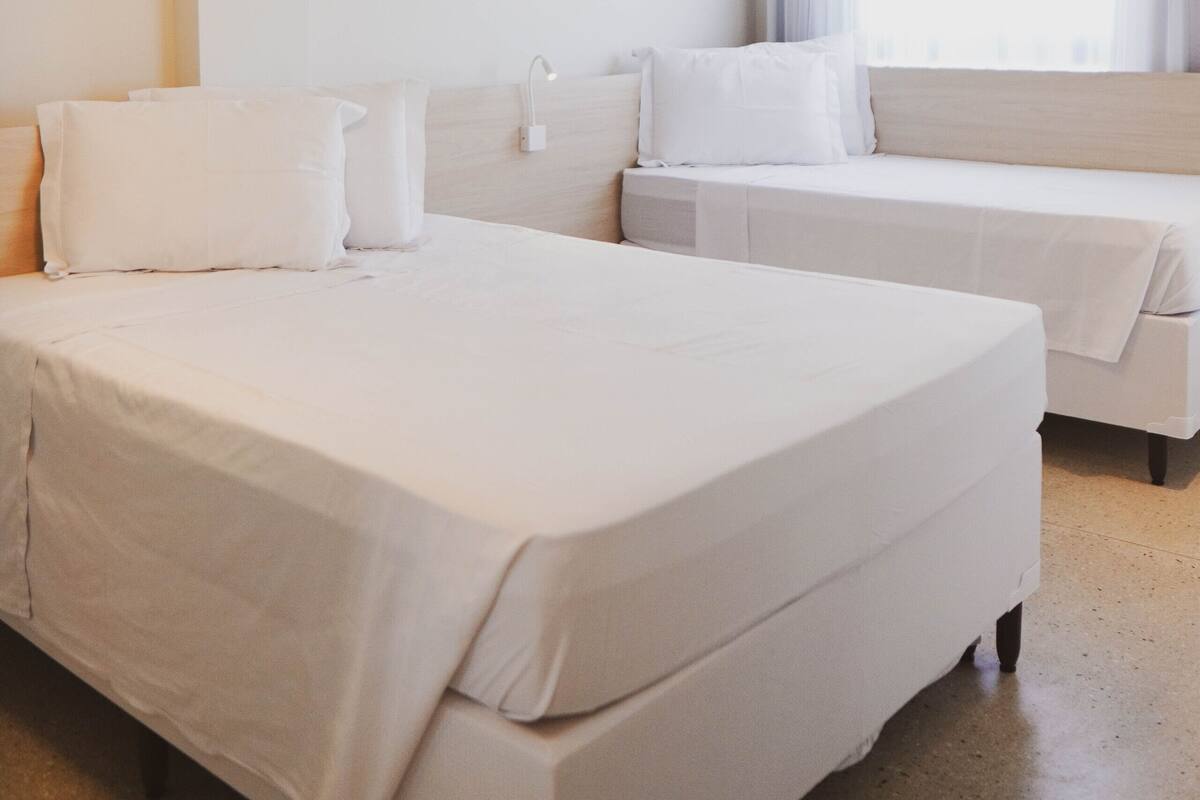 Una habitación de hotel con una cama grande, una cama más pequeña y una ventana con cortinas.