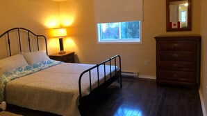 A bedroom with a bed, bedside lamp, dresser, window, and a mirror on the wall.