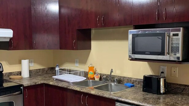 A kitchen with dark wooden cabinets, a stainless steel dishwasher, a microwave, a toaster, and a granite countertop.