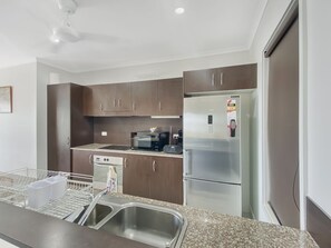 A modern kitchen with stainless steel appliances, dark wooden cabinets, and a granite countertop. - Magnetic Docks Townhouse 8 (Nelly Bay)