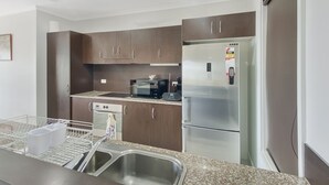A modern kitchen with stainless steel appliances, dark wooden cabinets, and a granite countertop. - Magnetic Docks Townhouse 8 (Nelly Bay)