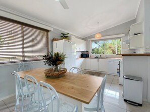 A modern kitchen with white cabinetry, a wooden dining table, and a view of the outdoors through large windows.