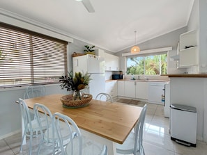 A modern kitchen with white cabinetry, a wooden dining table, and a view of the outdoors through large windows. - Magnetic Haven Unit 7 (Arcadia)
