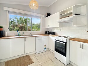 A modern kitchen with white cabinets, a built-in oven, a dishwasher, and a window with a view of greenery.