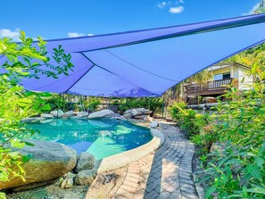 A swimming pool with a curved edge, surrounded by rocks and plants, under a blue canopy. - Magnetic Haven Unit 7 (Arcadia)