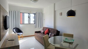 Een moderne woonkamer met een bank, een glazen tafel en een aan de muur bevestigde televisie.