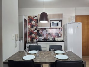 Une cuisine moderne équipée d’un four à micro-ondes, d’une cuisinière et d’un réfrigérateur, une table à manger dressée avec des assiettes et des verres, et un pare-feu orné d’un motif géométrique.