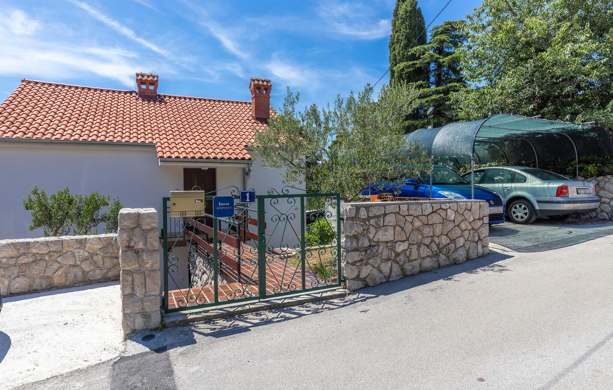 A residential property with a red-tiled roof, a stone wall, and a metal gate.