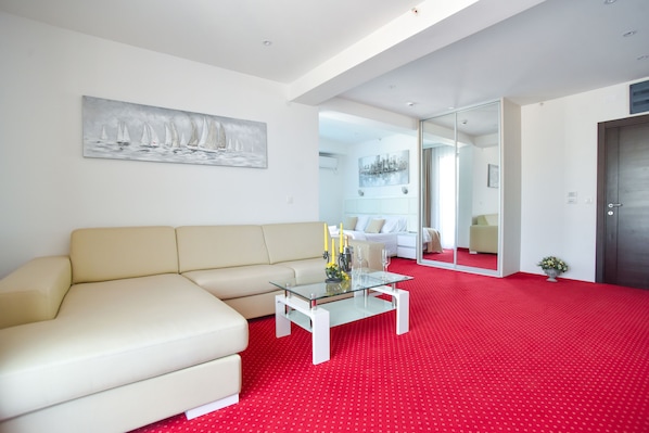Una sala moderna con un sofá color beige, una mesa de centro de vidrio y una alfombra roja.