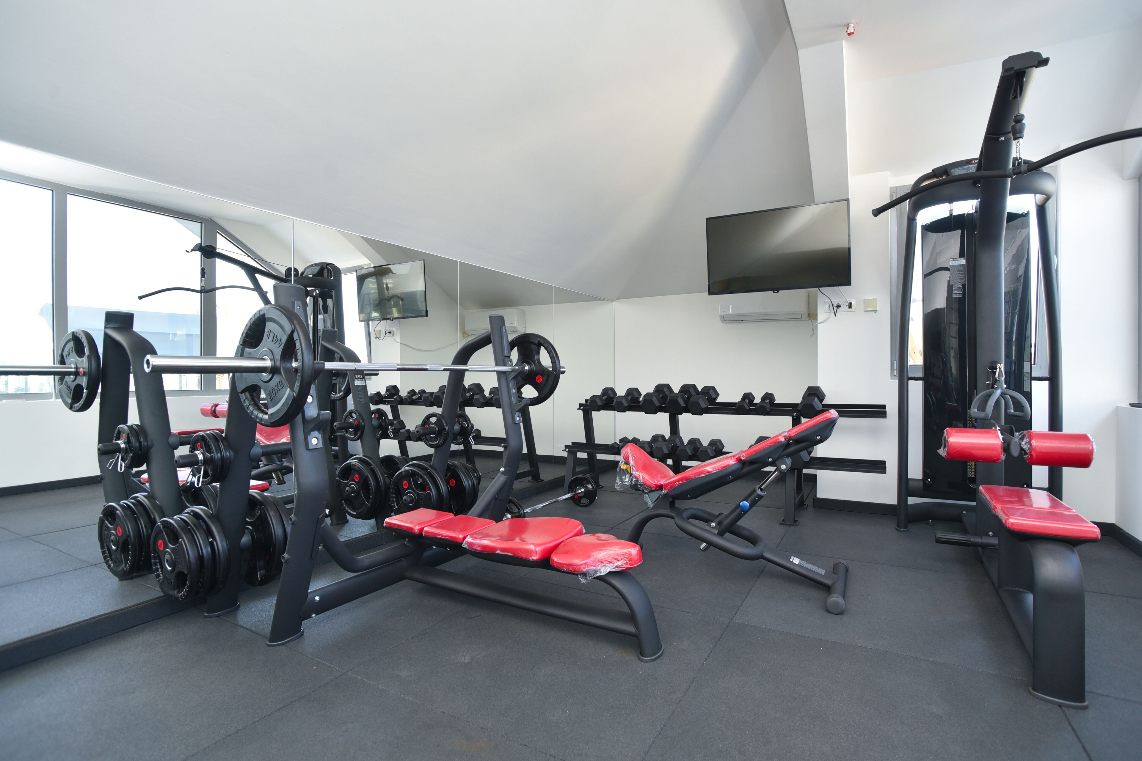 Un gimnasio con diverso equipamiento de ejercicio, que incluye mancuernas, bancos y máquinas de pesas.