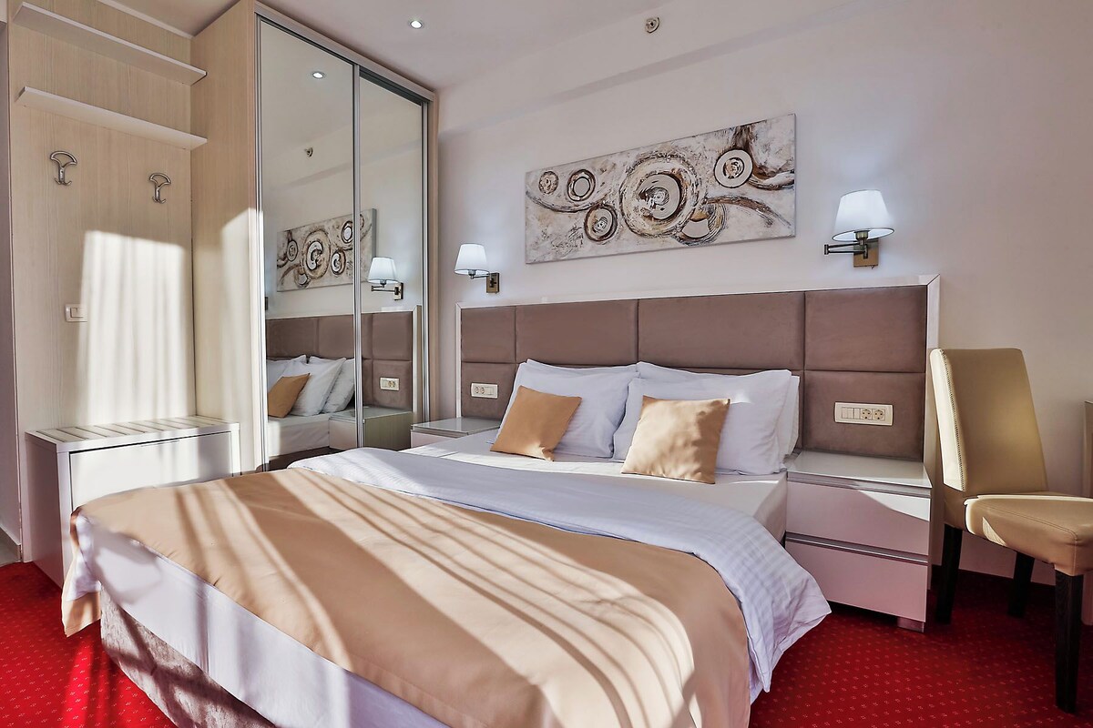 Une chambre d’hôtel avec un grand lit, une table de chevet, une chaise, un miroir et une œuvre d’art accrochée au mur.