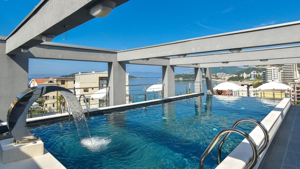 Una piscina infinita con un cielo azul despejado de fondo, un diseño arquitectónico moderno y vistas de la ciudad.