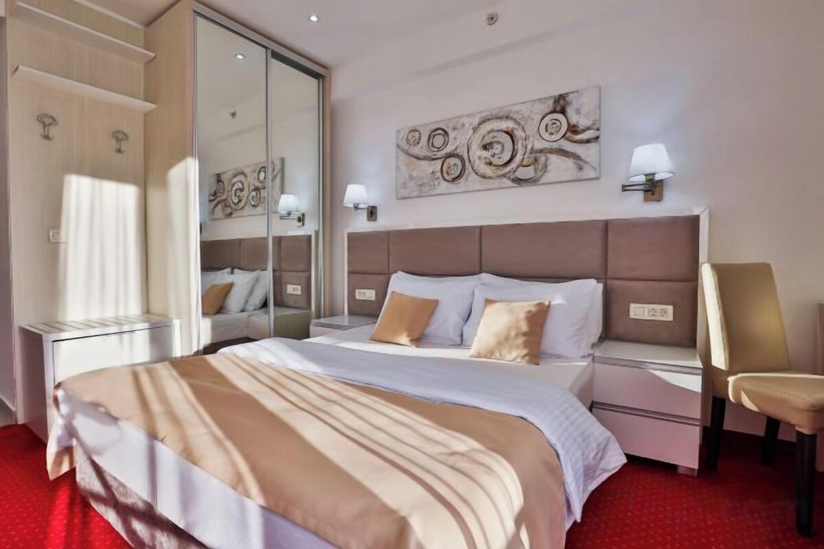 A hotel room with a large bed, a bedside table, a chair, a mirror, and artwork on the wall.