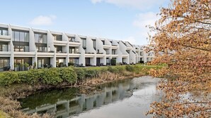 Ein modernes Gebäude mit einzigartigem architektonischen Design, das mehrere Balkone und ein reflektierendes Wasserelement vor der Fassade besitzt.