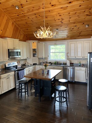 A spacious kitchen with wooden ceiling, white cabinets, a central island, and a hanging light fixture.