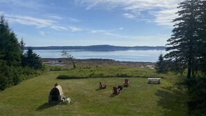 Un espacio con césped, una pequeña construcción de ladrillo, varias sillas Adirondack y una mesa de picnic.