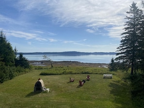 A grassy area with a small brick structure, several Adirondack chairs, and a picnic table.