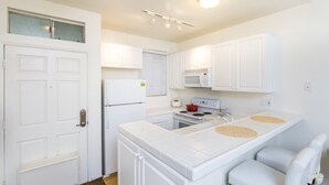 Une cuisine compacte avec des meubles blancs, un four à micro-ondes, une cuisinière et un petit réfrigérateur.