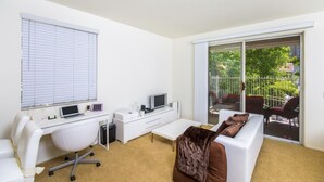 Un salon moderne avec un canapé blanc, un bureau avec un ordinateur et une grande porte-fenêtre coulissante donnant sur un balcon.