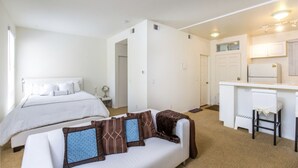 Une chambre d’hôtel de taille réduite comprenant un lit, un canapé, une petite kitchenette et une salle de bain.