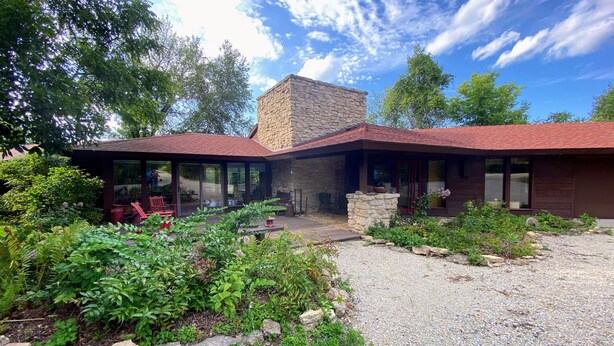Una casa moderna con chimenea de piedra, un patio con mobiliario exterior y un jardín bien cuidado.