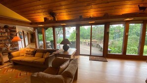 Un salón amplio con pisos de madera y ventanas grandes, un sofá, una mesa de centro y una estantería.