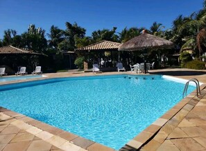 Ein klares, blaues Schwimmbecken mit Liegestühlen und strohgedeckten Sonnenschirmen.