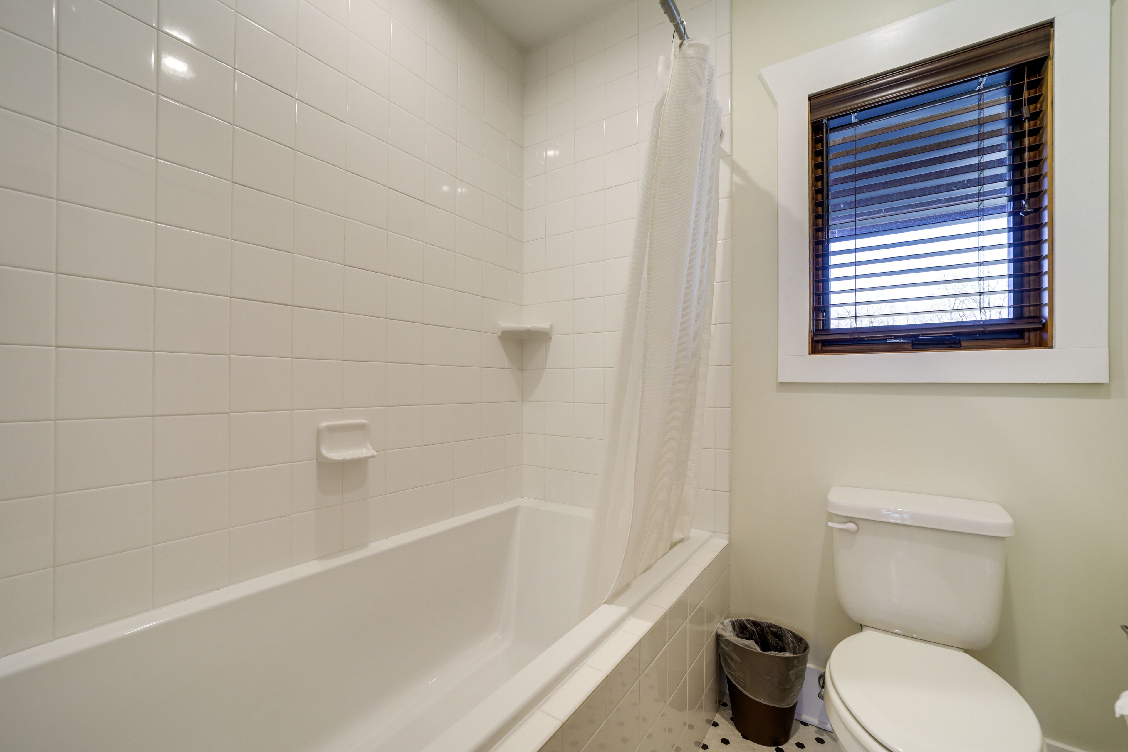 Un baño con bañera, inodoro y ventana con persianas.