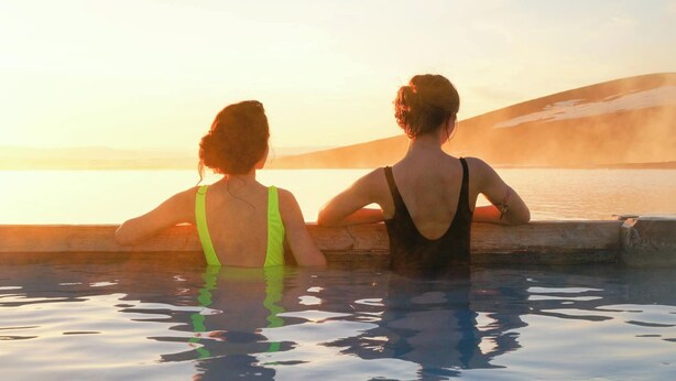 Dos personas sentadas junto a una piscina durante el atardecer.