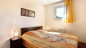 Ein Hotelzimmer mit einem großen Bett, einem Nachttisch mit Lampe, einem Fenster mit gelben Vorhängen und einem Wandbild.