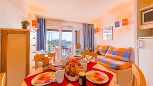 A dining area with a table set for two, a sofa, and a balcony view. - Studio Equipé 1.5km de la Plage (Le Barcarès)