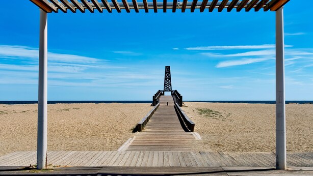 A wooden boardwalk leading to a pier with a lattice structure, surrounded by a sandy beach and clear blue sky. - Appart Abordable avec Terrasse Privée (Le Barcarès)