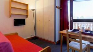 Een kamer met een bed, een bureau met stoel, een kast, een televisie en een raam met uitzicht.