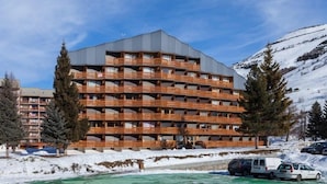 Een hotel met meerdere verdiepingen, balkons, een zwembad en een besneeuwde berg op de achtergrond.