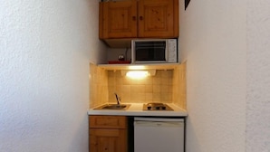 Een kleine keuken met houten kastjes, een magnetron, een spoelbak en een vaatwasser.