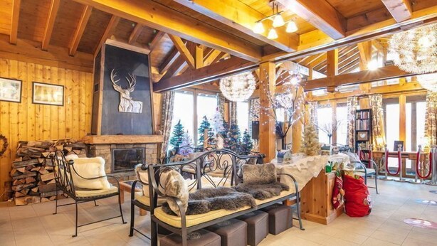 A cozy lodge interior with a fireplace, wooden walls, a sofa with fur throw pillows, and Christmas decorations. - Apt Equipé | Au Pied des Pistes + Parking Gratuit (Doucy)