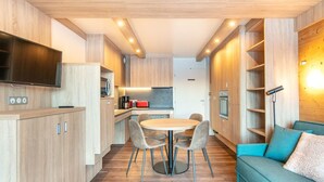 A modern kitchen with wooden cabinets, a dining table with chairs, and a built-in TV. - Apt Equipé | Au Pied des Pistes + Parking Gratuit (Doucy)