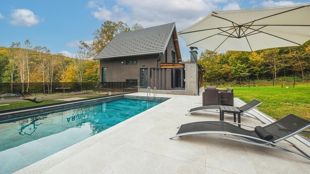 A modern house with a swimming pool, outdoor seating, and a large umbrella.