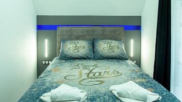 Een netjes opgemaakt bed met een sterrenprint deken en kussens, twee handdoeken op het bed, en een modern hoofdbord met ingebouwde verlichting.