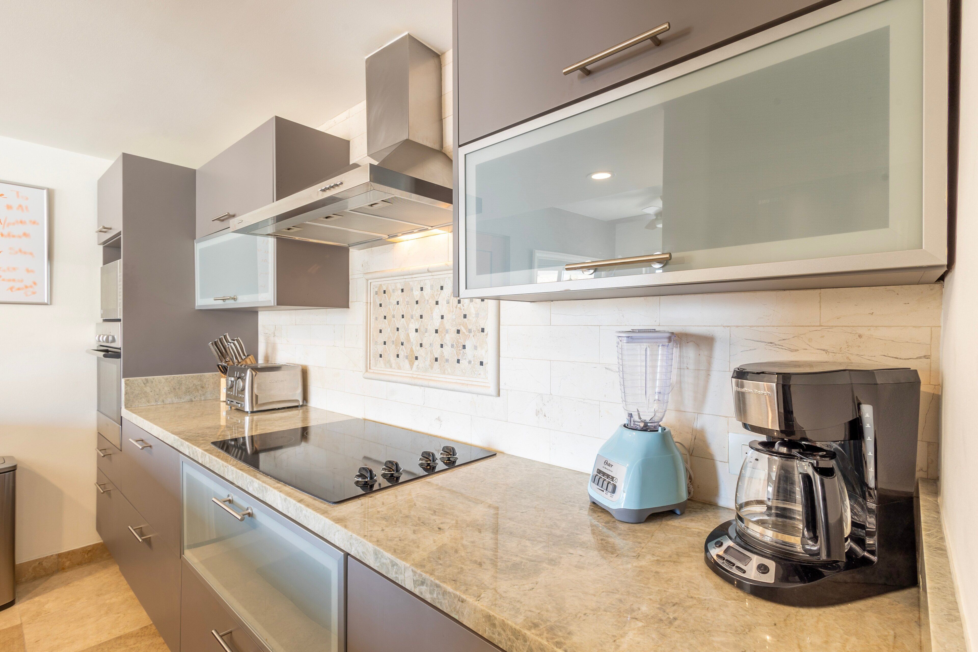 A modern kitchen with grey cabinets, a black coffee maker, and a blender on the countertop.