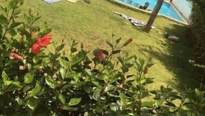 Un immeuble résidentiel doté d’une piscine, entouré d’une pelouse et de quelques plantes.