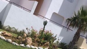Un bâtiment à l’extérieur blanc, doté d’un balcon et d’un petit jardin agrémenté de rochers et de plantes.