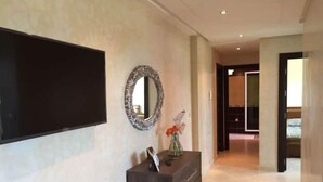 Un couloir avec un téléviseur à écran plat fixé au mur, un miroir décoratif et une commode en bois foncé dotée de tiroirs.