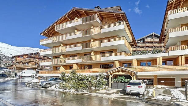 Un hôtel à plusieurs étages, doté de balcons en bois, avec une piste de ski en arrière-plan.